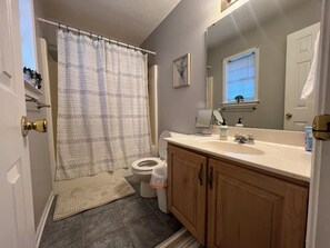 A bathroom with a shower curtain, toilet, sink, and wooden cabinets.