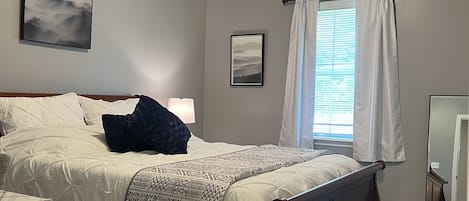 Ein Schlafzimmer mit einem Bett, einem Deckenventilator, einem Fenster mit Vorhängen und einem an der Wand befestigten Spiegel.