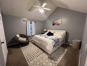 A bedroom with a bed, a chair, a ceiling fan, a window with curtains, and a rug.