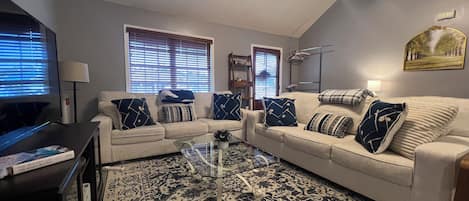 A living room with a beige sofa, a glass coffee table, and a patterned rug.