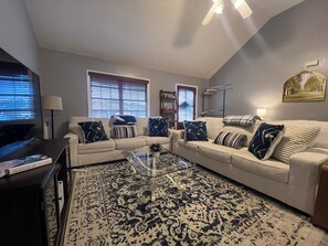 A living room with a beige sofa, a glass coffee table, and a patterned rug.