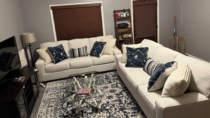 Ein Wohnzimmer mit zwei Sofas, einem Couchtisch, einer Lampe, einem Bücherregal und einem gemusterten Teppich.