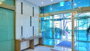A reception area with a glass door entrance, a reception desk, and a blue carpet leading outside. - mir hotel (Sokcho)