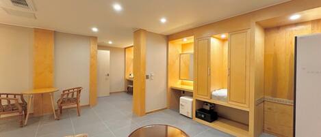 A hotel room with a wooden vanity, a small table, two armchairs, and a bed.