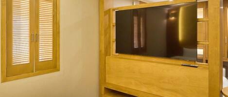 Ein Schlafzimmer mit einem HolztV-Möbel, einem Bett und einem Fenster mit Jalousien.