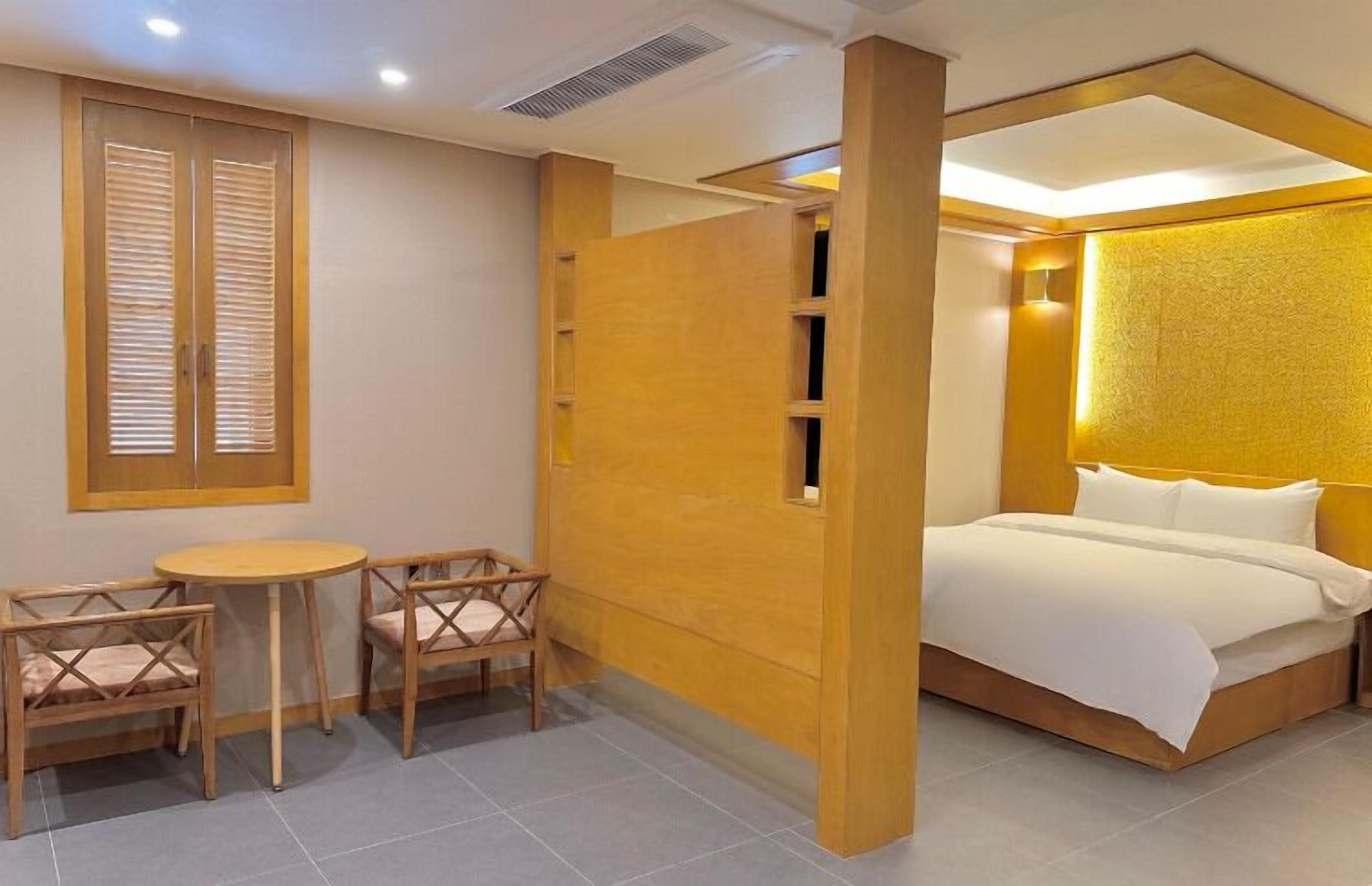 A hotel room with a bed, a small table, two chairs, and a wooden partition.