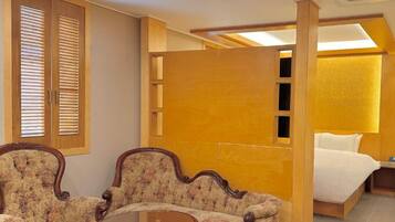 Habitació d'hotel amb un llit, dues butaques tapissades, una taula rodona petita i una separació de fusta.