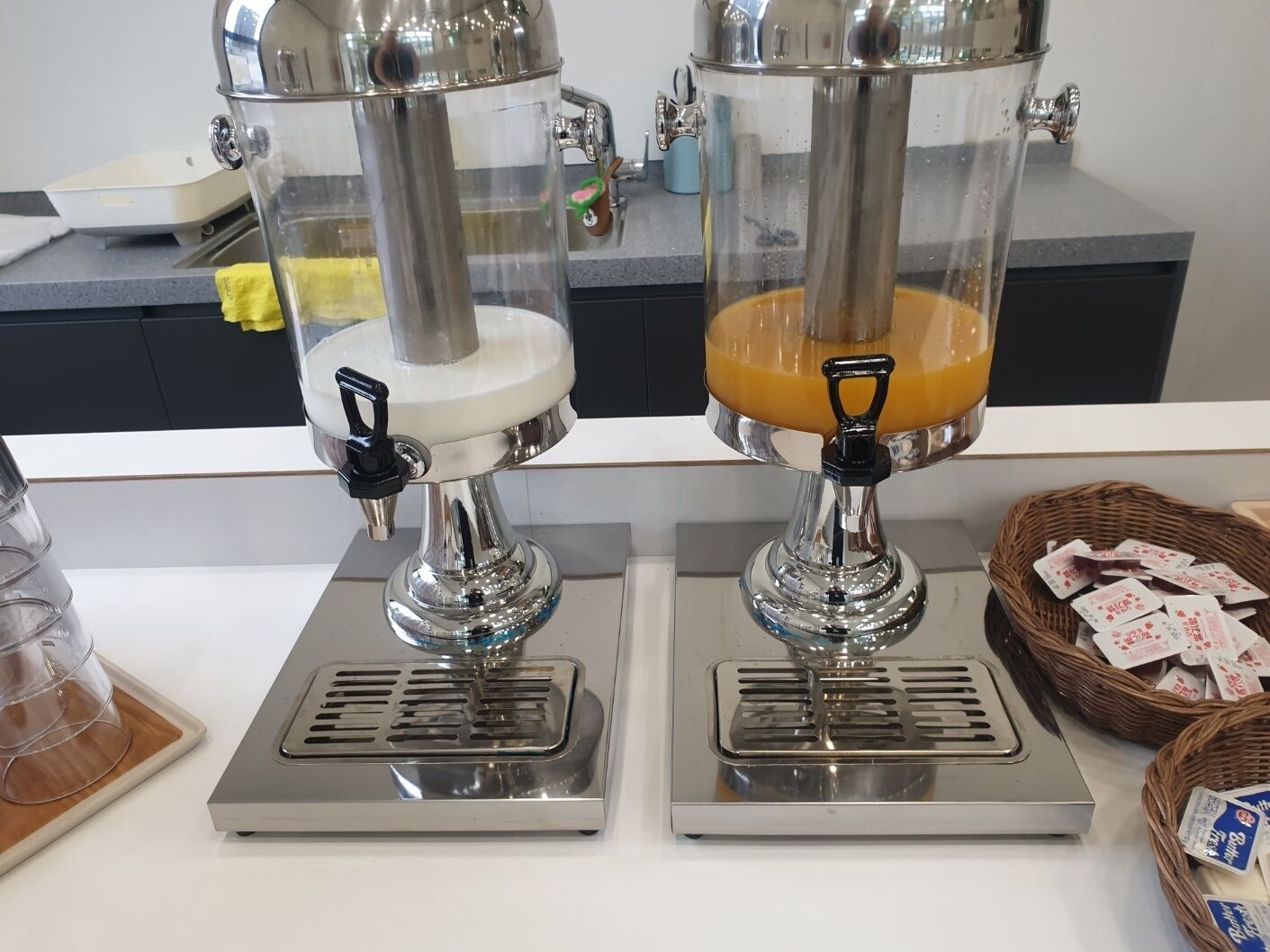 Dos dispensadores de bebidas de acero inoxidable con recipientes transparentes, colocados sobre una encimera.