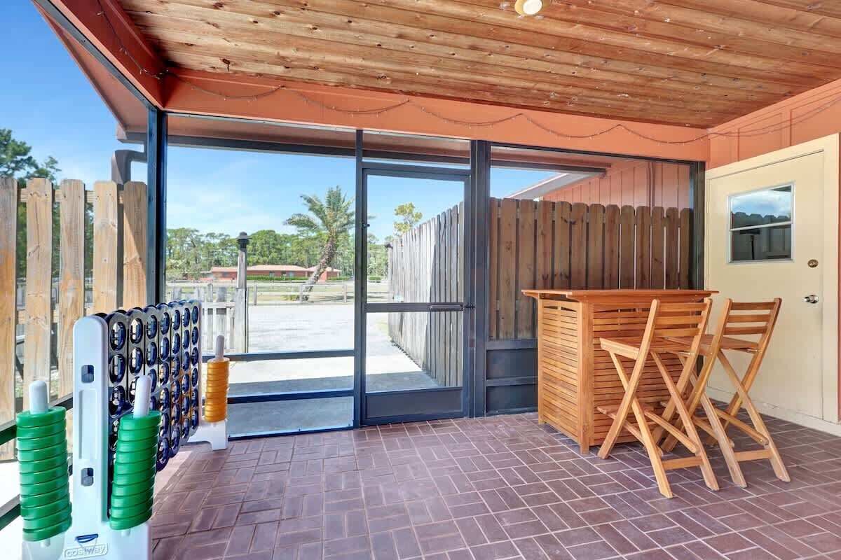 Un patio cubierto con mesa y sillas de madera, una puerta que da al exterior, y un perchero con objetos.
