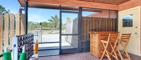 Un patio cubierto con mesa y sillas de madera, una puerta que da al exterior, y un perchero con objetos.