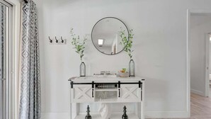 Une console blanche, surmontée d’un miroir rond, avec deux petites plantes en pot et un jeu d’échecs posé sur l’étagère inférieure.