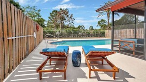 Un espace aménagé au bord de la piscine, avec des chaises longues en bois, une piscine et une clôture en bois.