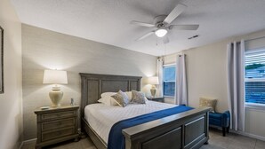 Une chambre à coucher avec un lit, des tables de chevet, un ventilateur de plafond et une fenêtre avec des rideaux.