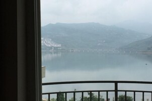 Vista desde un balcón sobre un lago tranquilo, con montañas a lo lejos y un puente en el centro.