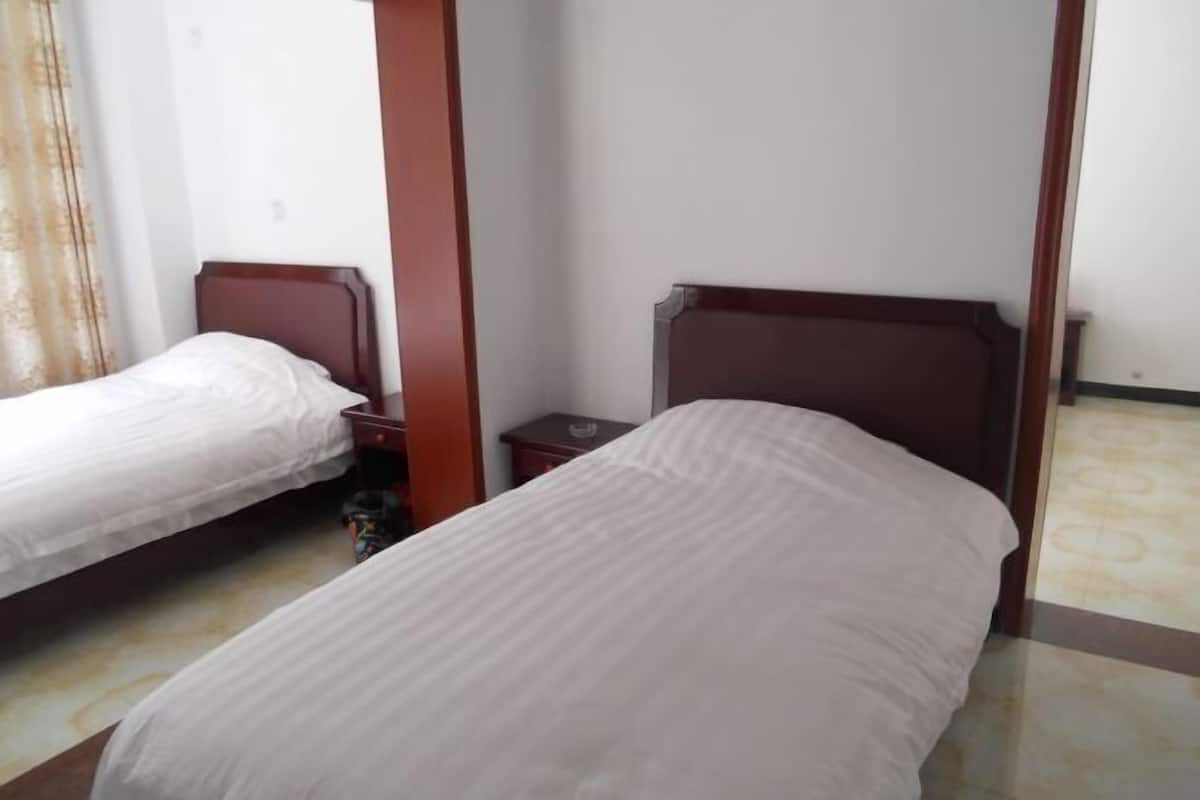 A hotel room with two single beds, a wooden headboard, a small nightstand, and a tiled floor.