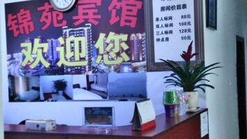 A hotel reception desk with a clock, a menu board, and a potted plant.