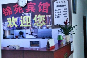 A hotel reception desk with a clock, a menu board, and a potted plant.