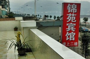 Letrero de hotel con caracteres chinos, una planta en maceta y vista de un paisaje urbano con montañas al fondo.