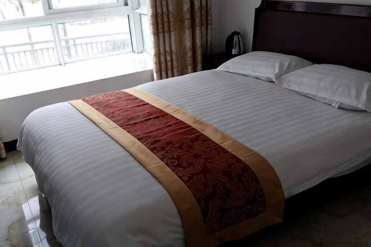 A hotel room with a bed, a window with curtains, and a nightstand.