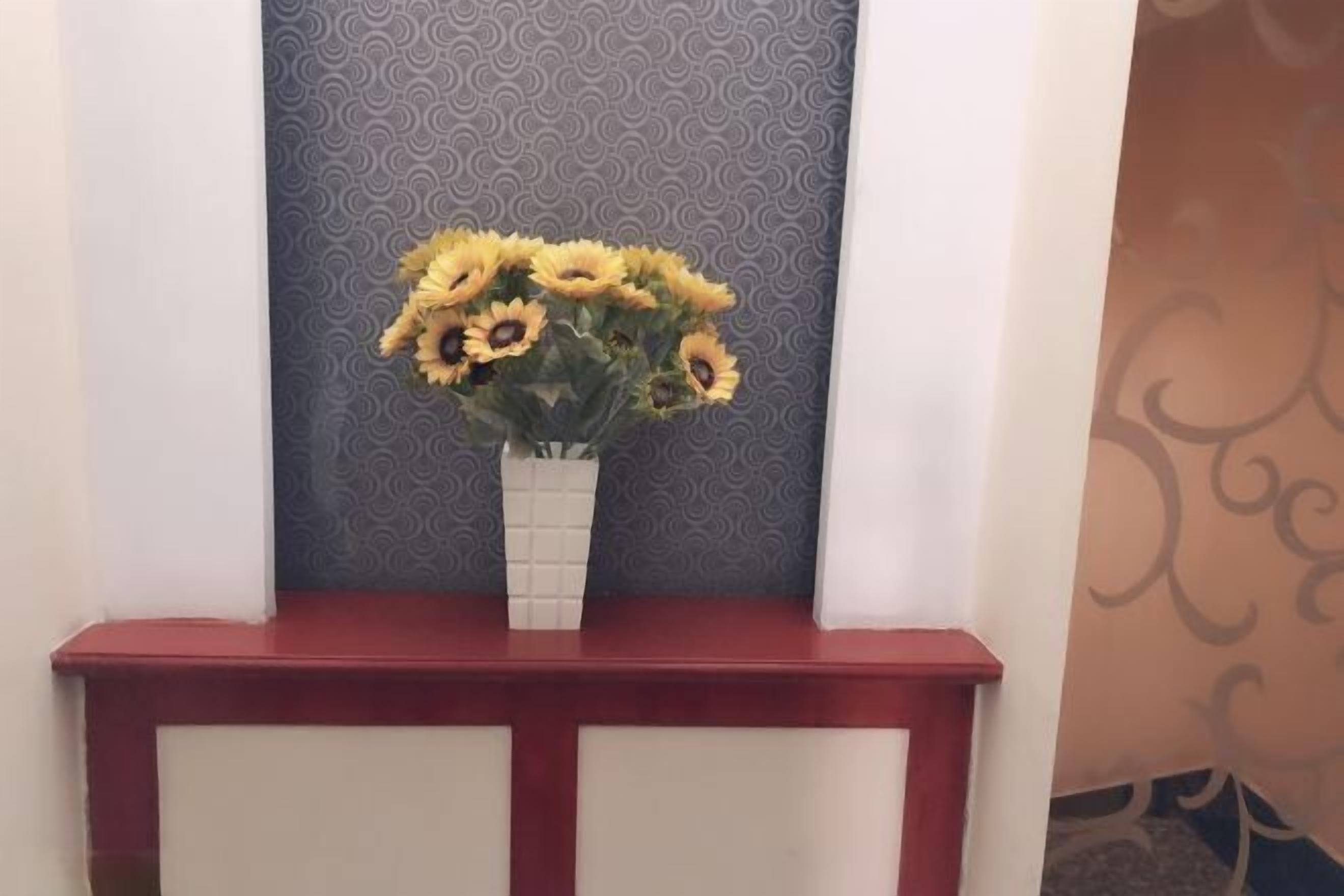A red console table with a white vase containing sunflowers.