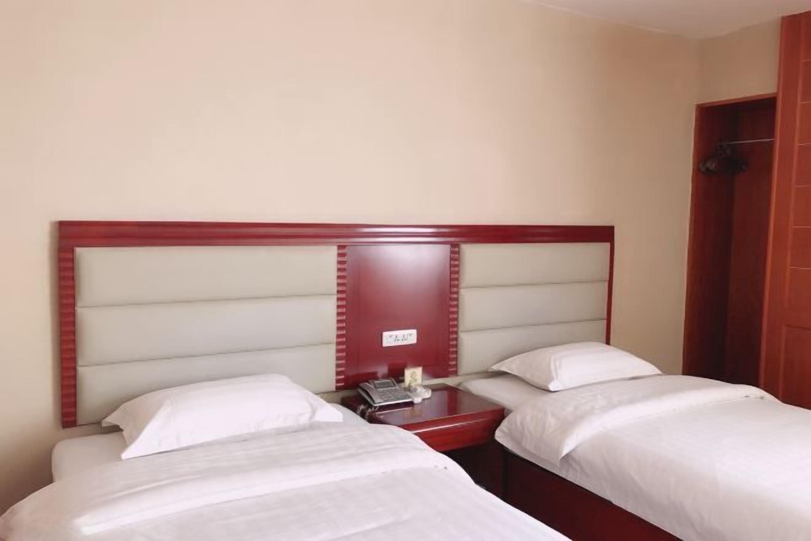 A hotel room with two single beds, a wooden headboard, a small bedside table with a phone, and a red door.