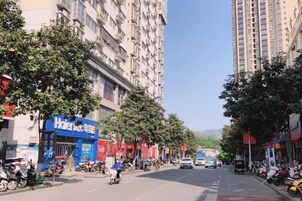 Una calle con un edificio azul identificado como 'Hotel' a la izquierda, rodeado de árboles y scooters estacionados.