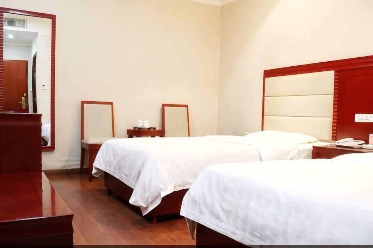 Ein Hotelzimmer mit zwei Betten, einem Holzschrank, einem Spiegel und einem Nachttisch.