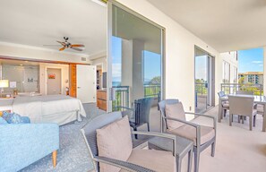 Una camera d'hotel con balcone, un letto, una poltrona e un'area pranzo con sedie.