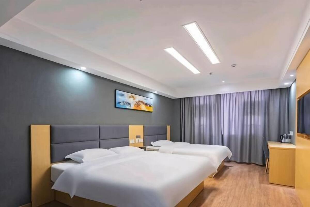 A hotel room with two beds, a desk, a chair, and a large window with curtains.