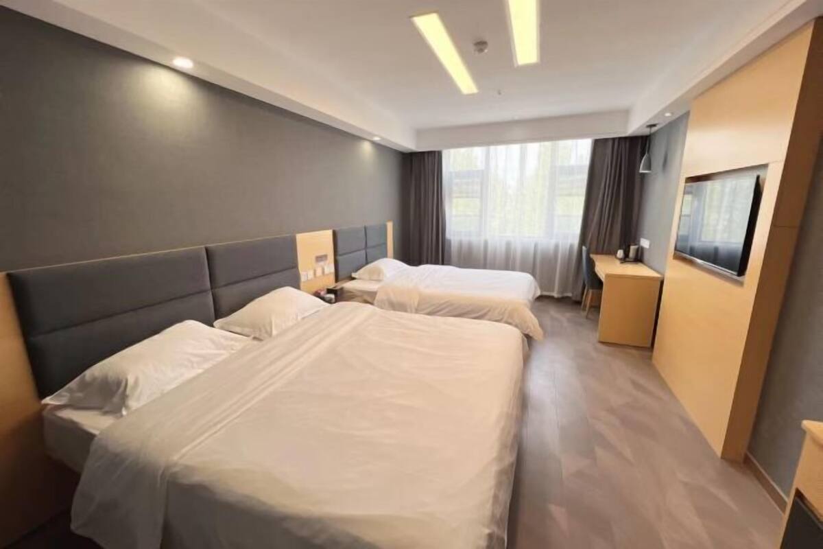 A hotel room with two beds, a desk, a chair, and a TV.