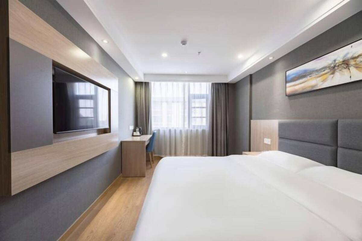 A modern hotel room with a large bed, a desk, a flat-screen TV, and a painting on the wall.