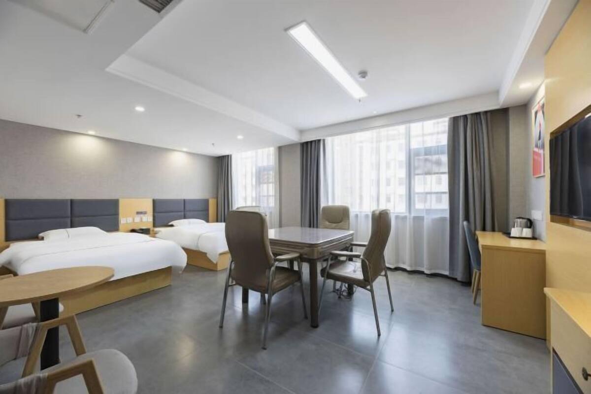 A hotel room with two beds, a dining table with chairs, a TV, and a desk.