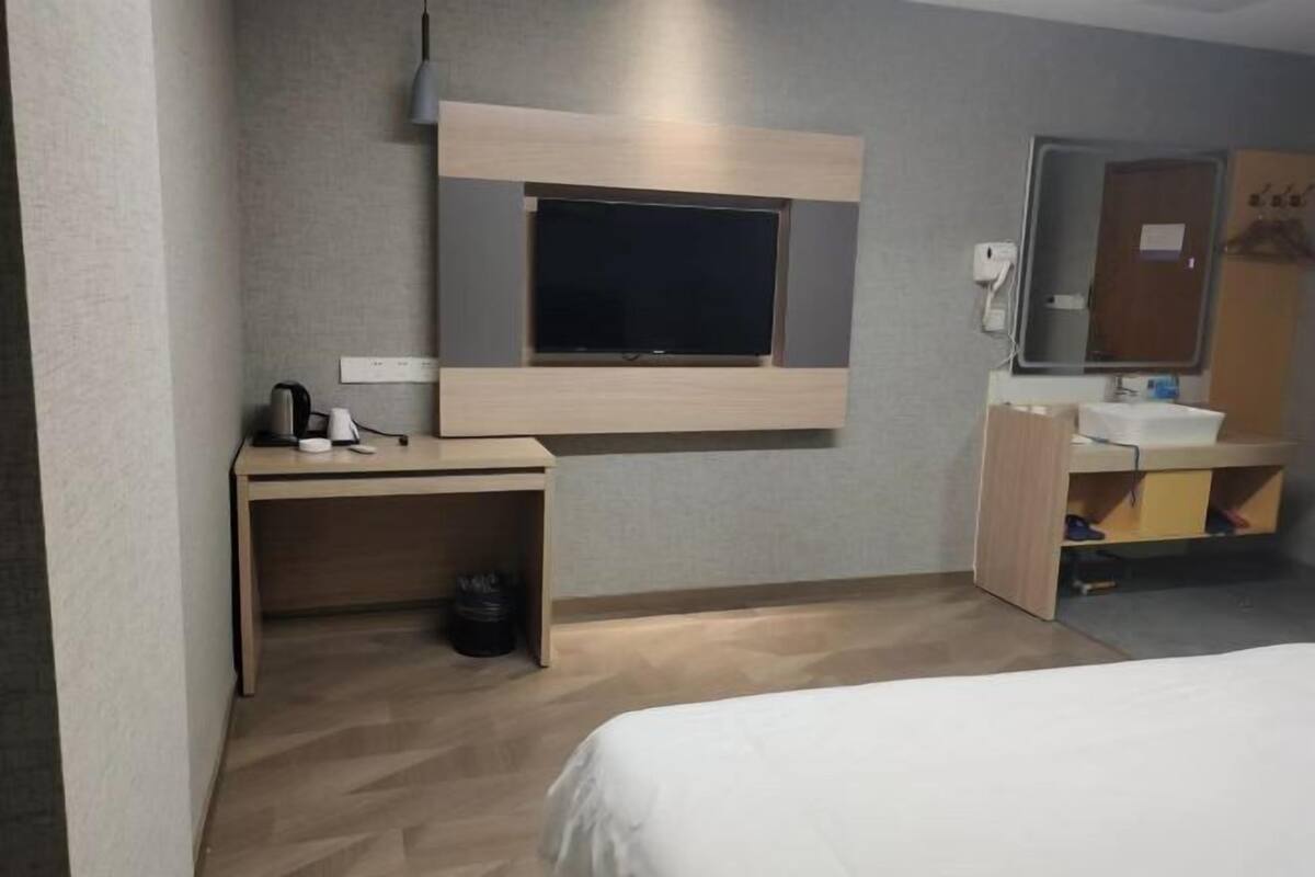 A hotel room with a bed, a desk with a television, a mirror, and a sink.