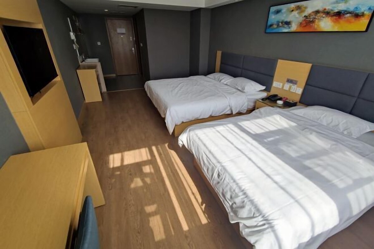 A hotel room with two beds, a TV, a desk, and a painting on the wall.