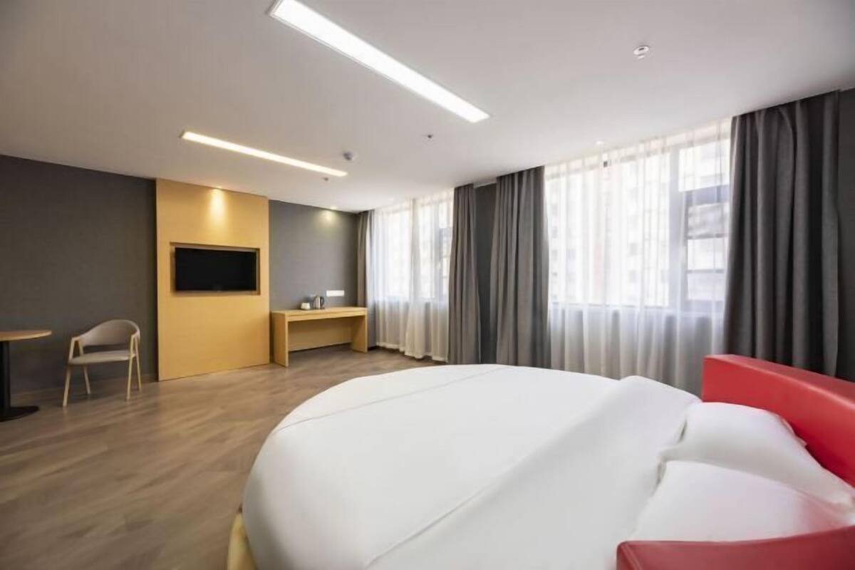 A modern hotel room with a large bed, a desk, a chair, and a TV.