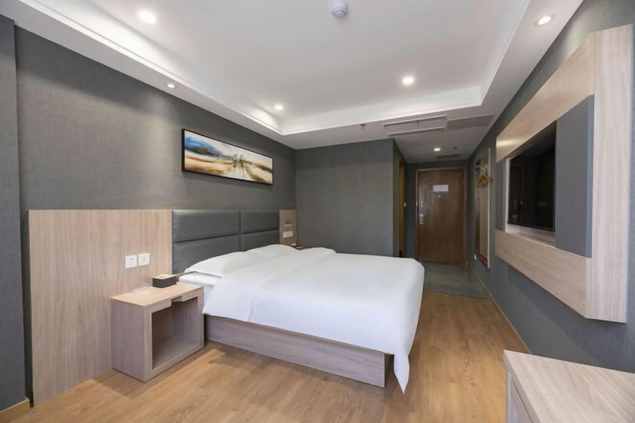 Una habitación de hotel moderna con una cama grande, una mesita de noche, un televisor montado y un cuadro en la pared.