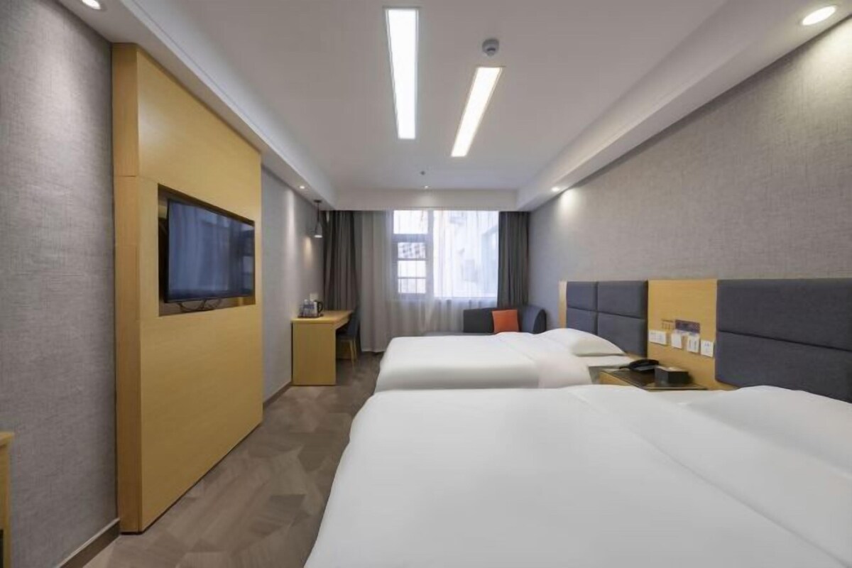 A hotel room with two beds, a desk, a television, and a window.