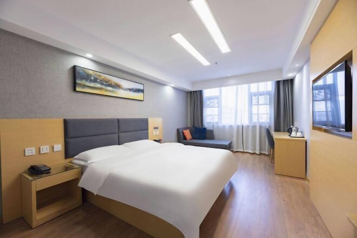 A hotel room with a bed, bedside table, lamp, and a painting on the wall.