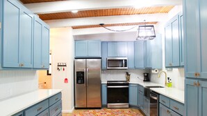 A kitchen with blue cabinets, stainless steel appliances, and a wooden ceiling.