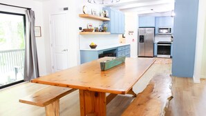 A spacious kitchen with a wooden table and benches, blue cabinets, and a stainless steel refrigerator.