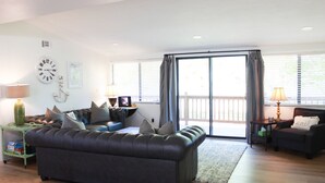 A modern living room with a dark leather sofa, a side table with a lamp, a small table with a lamp, and a view through large sliding glass doors.