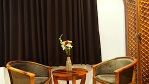 A room with two wooden armchairs, a small round table, and a vase with flowers. - Hotel Mewar Mahal - Udaipur (Udaipur)