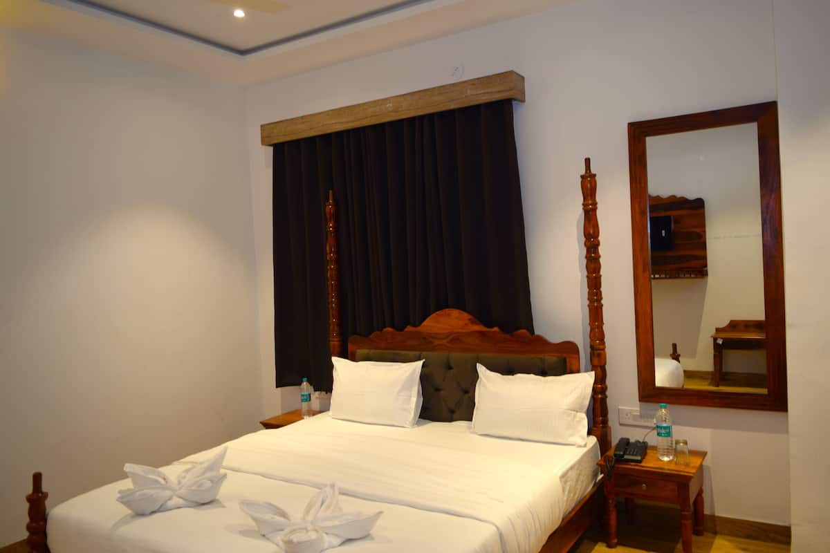 A neatly made bed with white linens and decorative towels, a wooden headboard, a bedside table with a bottle and a phone, and a mirror on the wall.