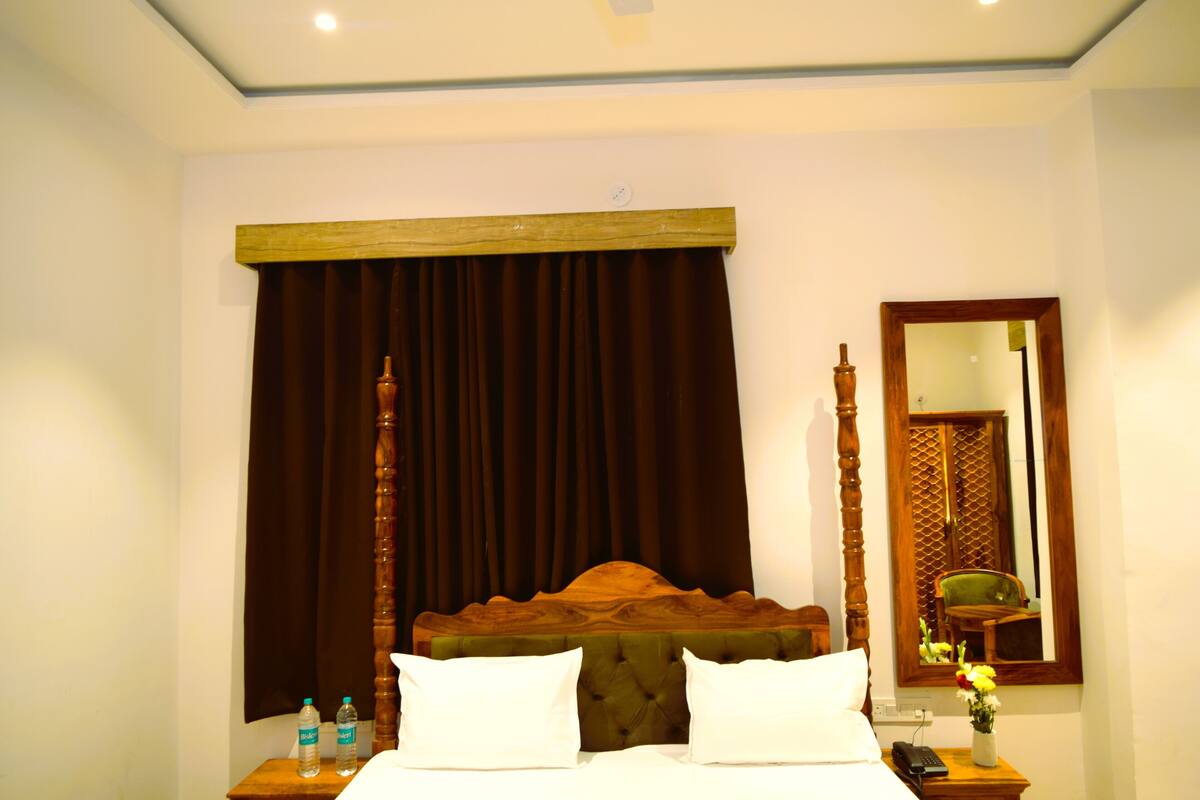 A hotel room with a wooden four-poster bed, a large mirror, and a nightstand with a vase of flowers.