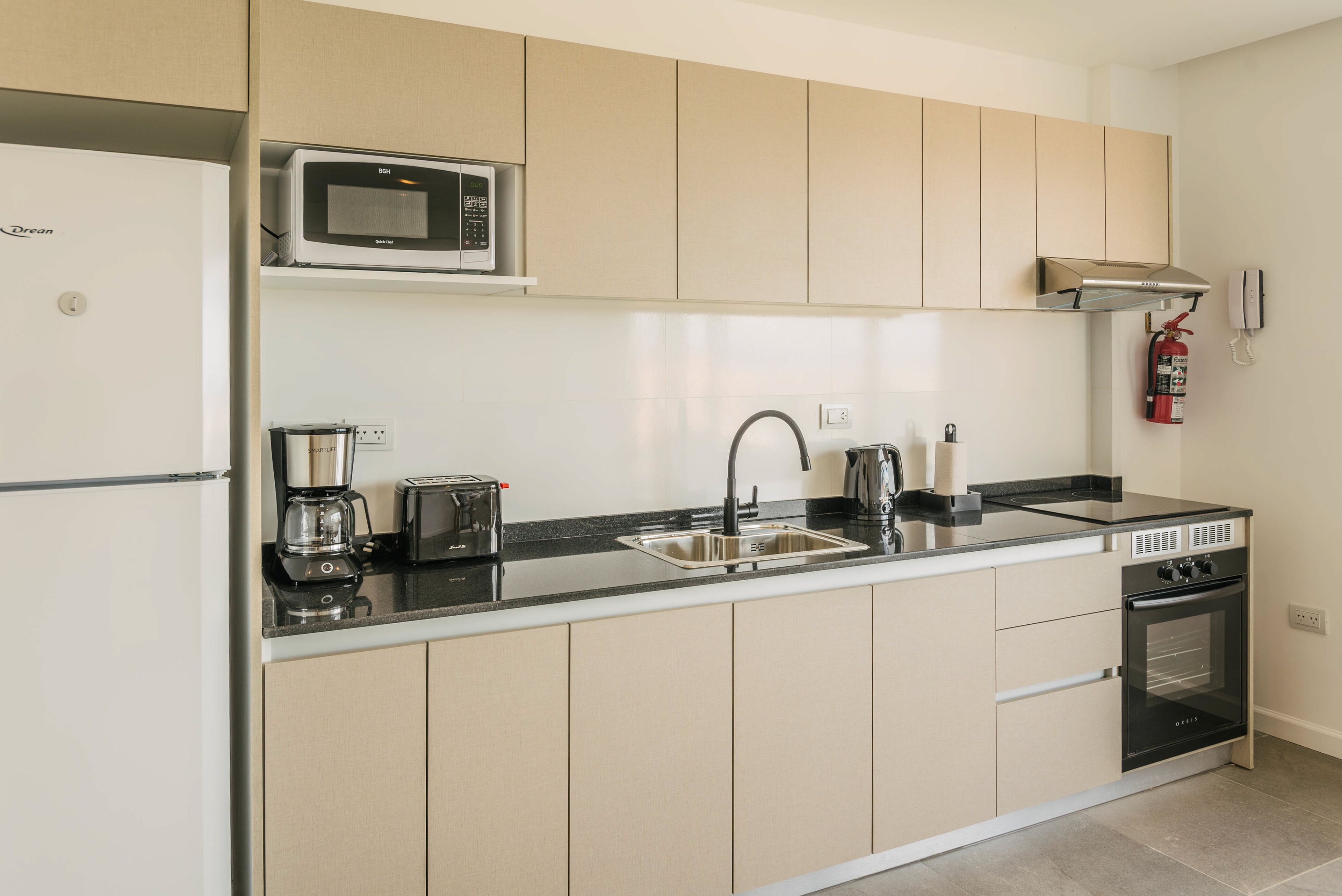 Uma cozinha compacta equipada com geladeira, micro-ondas, torradeira, pia, cafeteira e forno.