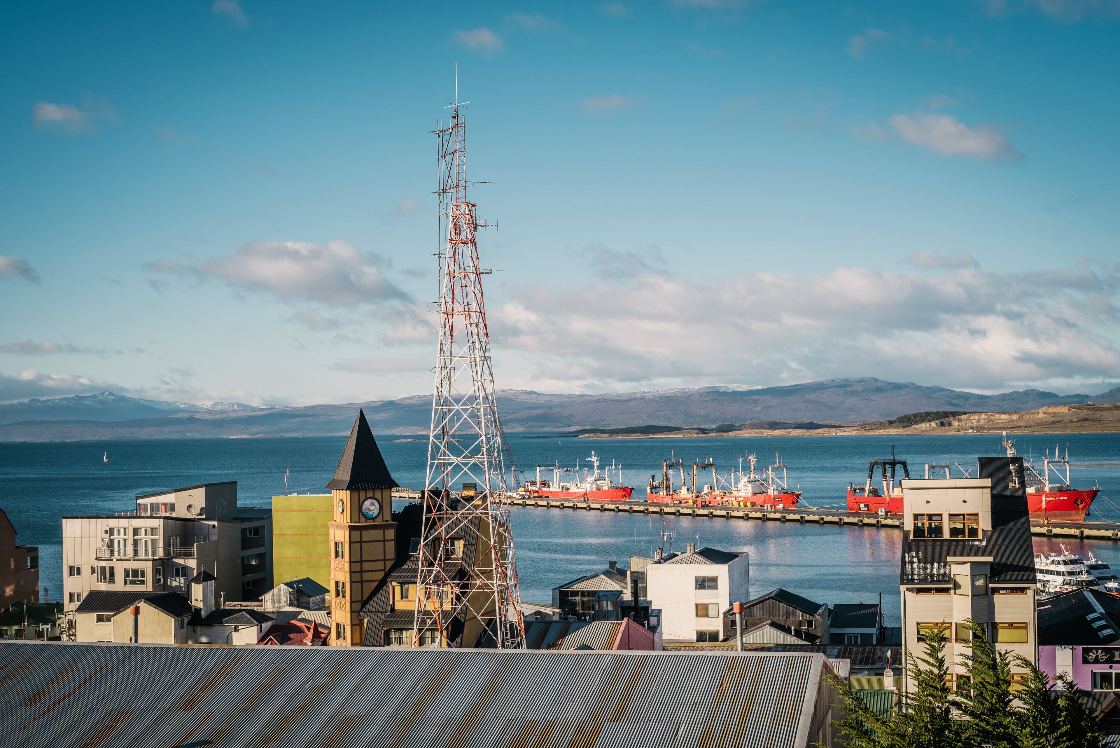 A coastal town with a prominent communication tower, a harbor with boats, and buildings with various architectural styles.
