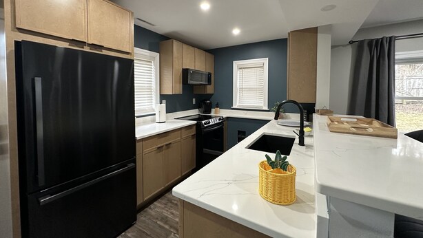 Eine moderne Küche mit einem schwarzen Kühlschrank, Holzschränken, einer weißen Arbeitsplatte und einer eingebauten Mikrowelle.