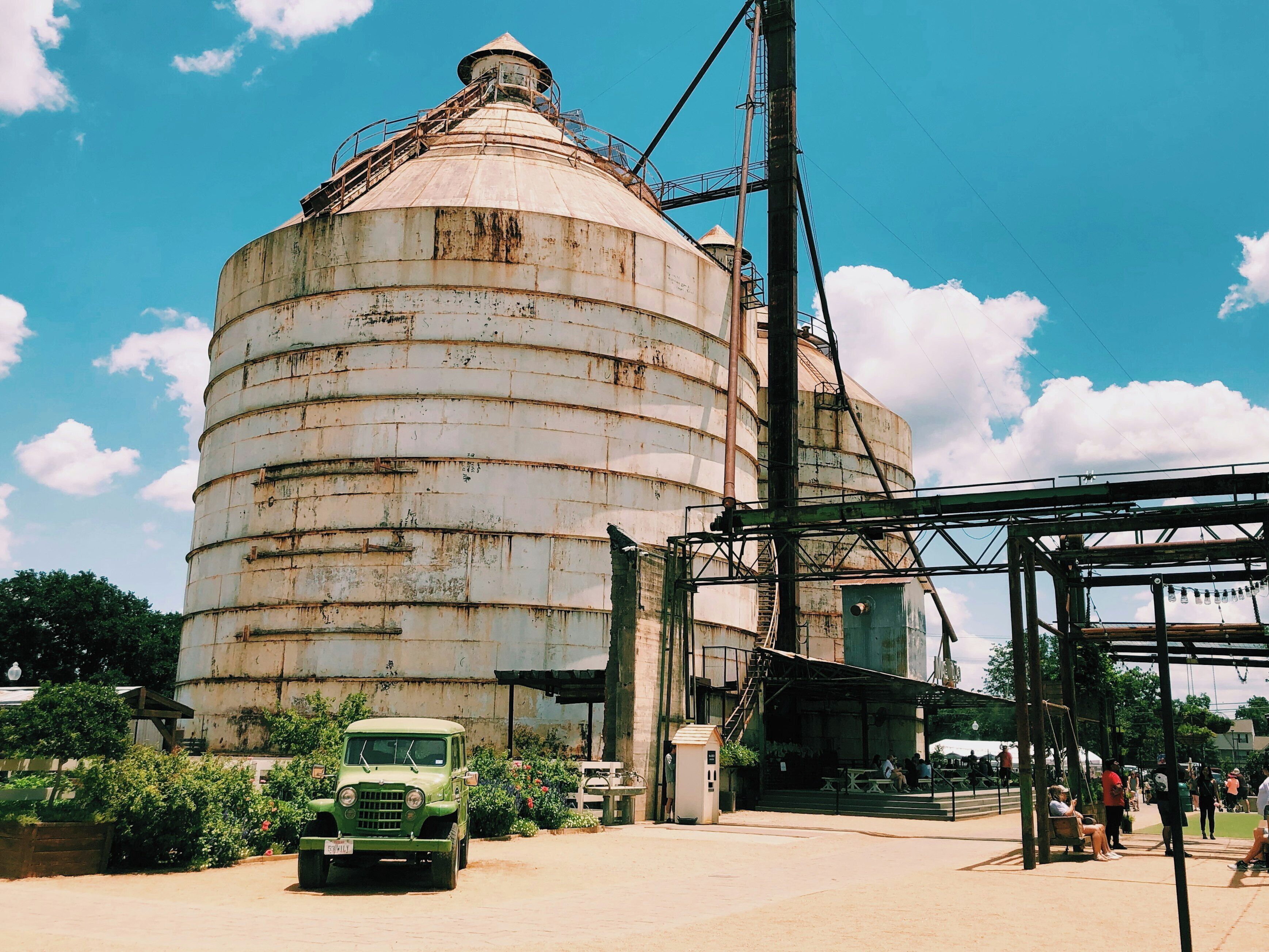 A large, rusted industrial silo with a green truck parked in front.