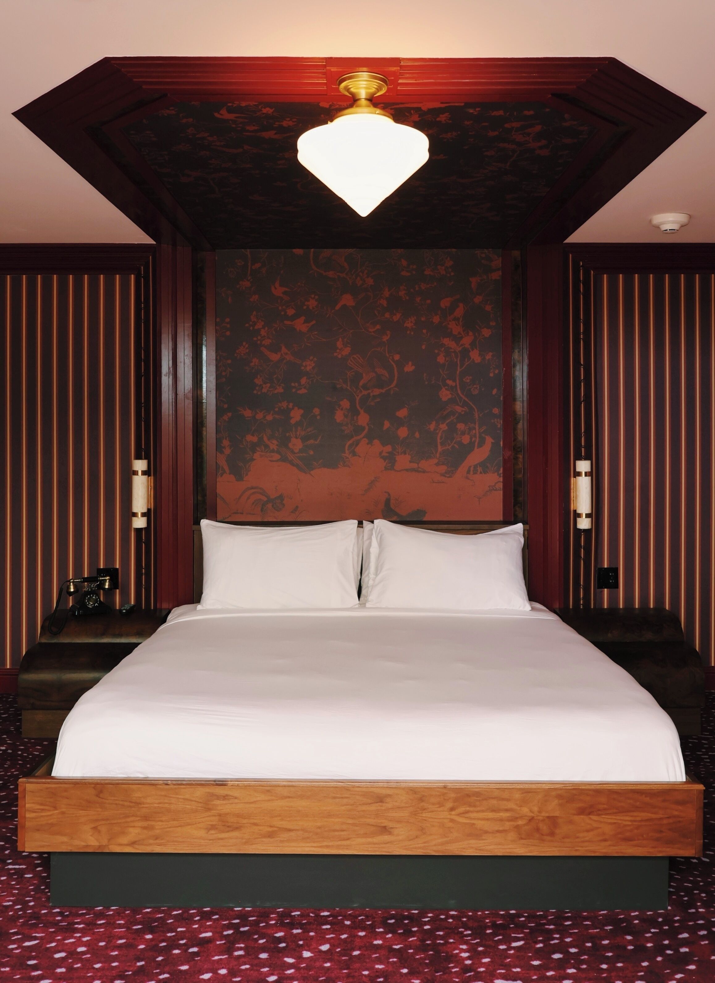 Habitación de hotel con una cama grande, un cabecero de madera, una pared con rayas rojas y una lámpara en el techo.