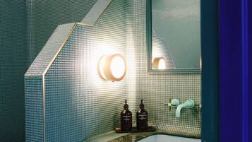 Une salle de bain avec un mur recouvert de carreaux verts, des toilettes blanches, un lavabo avec un miroir et un porte-serviettes.